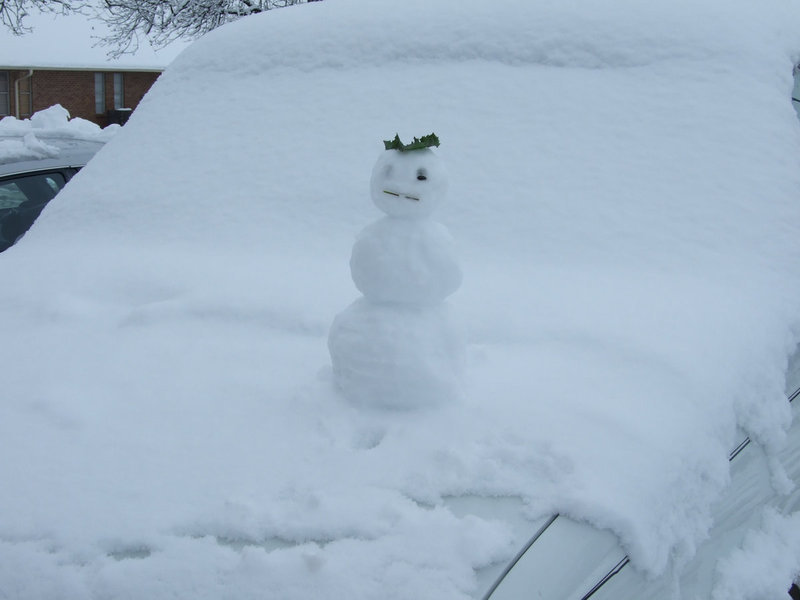 Image: Truck Snowman — This snowman was riding with his owner on the hood of the truck.  Amazing balance and strength, don’t you think?  It could have been the holly hat.