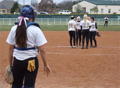 Image: Alyssa catches — Catcher Alyssa Richards stands behind home plate as the infield gathers at the mound for a pep talk.