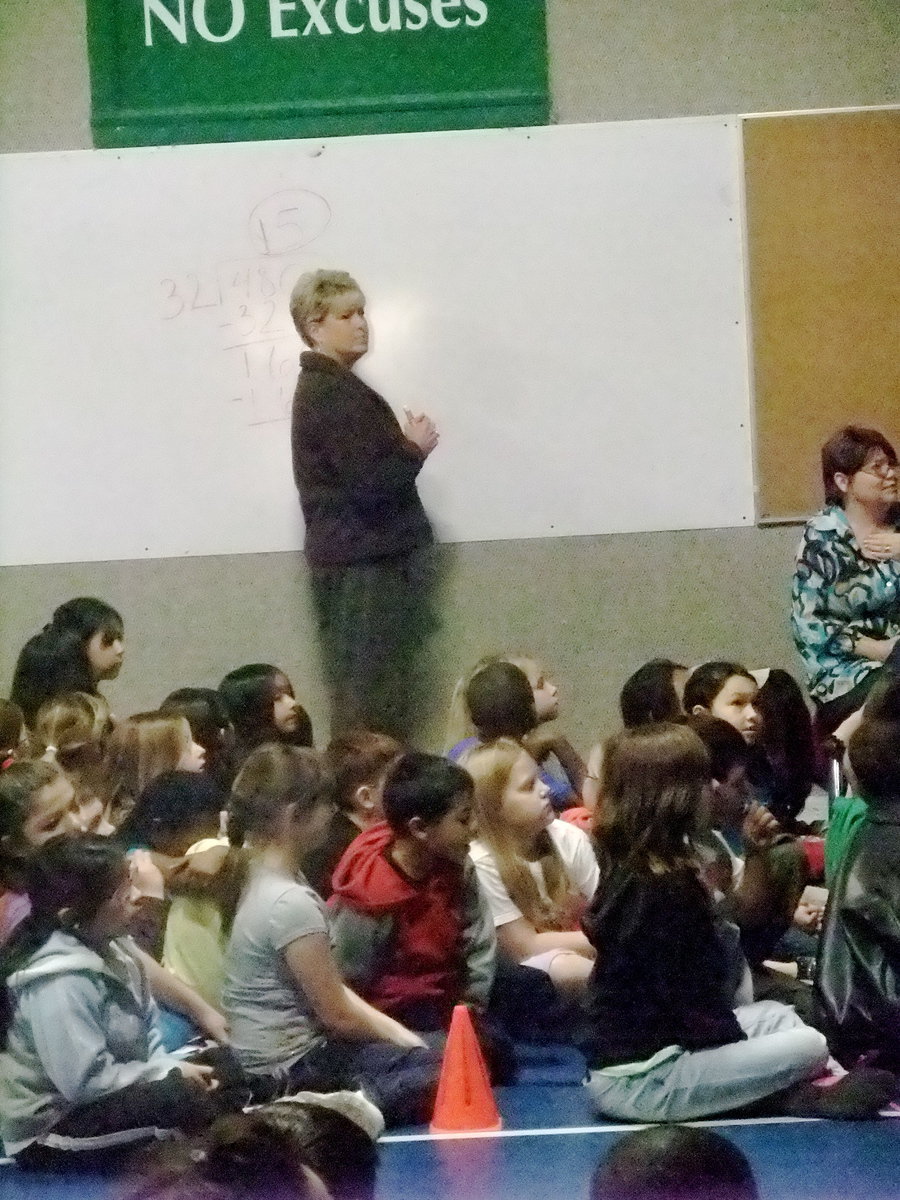 Image: Mrs. Prowell — Mrs. Prowell (teacher) invites the students to help her with her math problem. She is showing her work and explained to the students that they should do that too on the test.