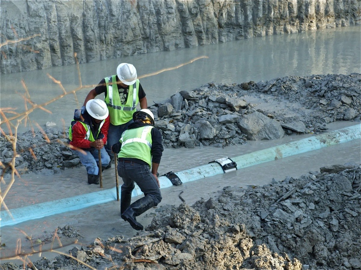 Image: 13 feet down — Three TTG crewmen use picks to shift the pipes.