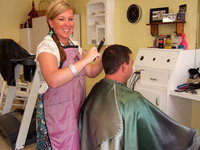 Image: Heather Cole and Customer — Heather is at Magic Mirror doing what she does best…hair! This young man is getting his hair cut by Heather and she is keeping him up with the times.