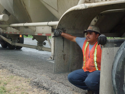 Image: Rain shade — Jesus Martinez takes cover from the rain under a separate 18-wheeler that was brought into haul away the cement mix.