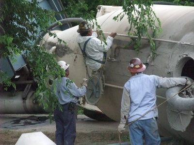 Image: Going in… — A volunteer climbs inside the sideways trailer to finish the removal of the cement mix.