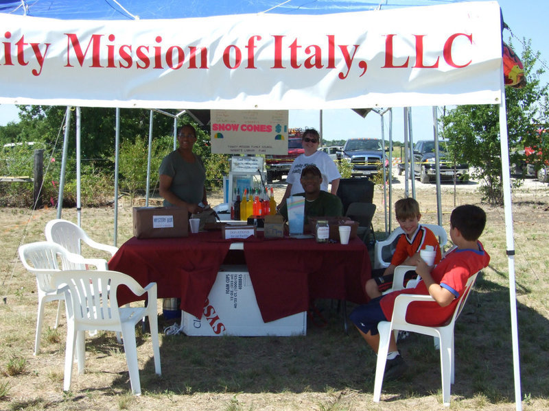 Image: Trinity Mission’s Booth — Volunteers Roslyn Baker, and Frankie Watson along with Chris Baker selling snow cones raising money for more books for the residents.