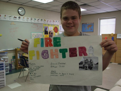 Image: William Youngblood — William Youngblood, one of Kelly’s students has this to say about Kelly Vernon, “She is nice to me and makes me learn.” He is holding up a report he did on fire fighters.