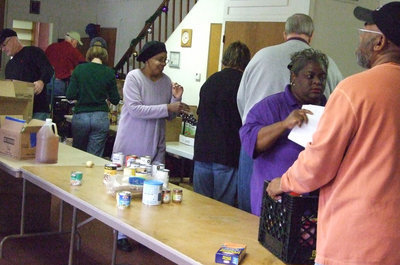 Image: Working hard — Juice, cereal, cranberry sauce and much, much more were donated to the IMA Food Pantry for local delivery.  Different churches were represented as volunteers worked together for Christmas.
