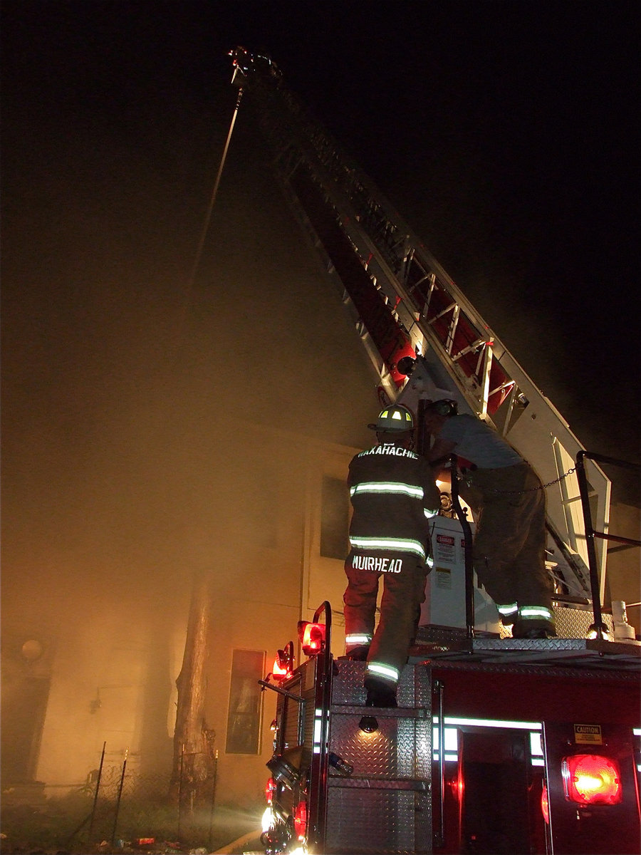 Image: The ladder truck — Waxahachie Fire Department Battalion Chief, Randy Muirhead, checks in with fellow firefighter, James Irvin, who is operating their Ladder 3 engine while battling the backside of Milford Cash Grocery during Tuesday night’s four-alarm blaze. Irvin, who originally had the day off, was called into action to man the extension ladder.