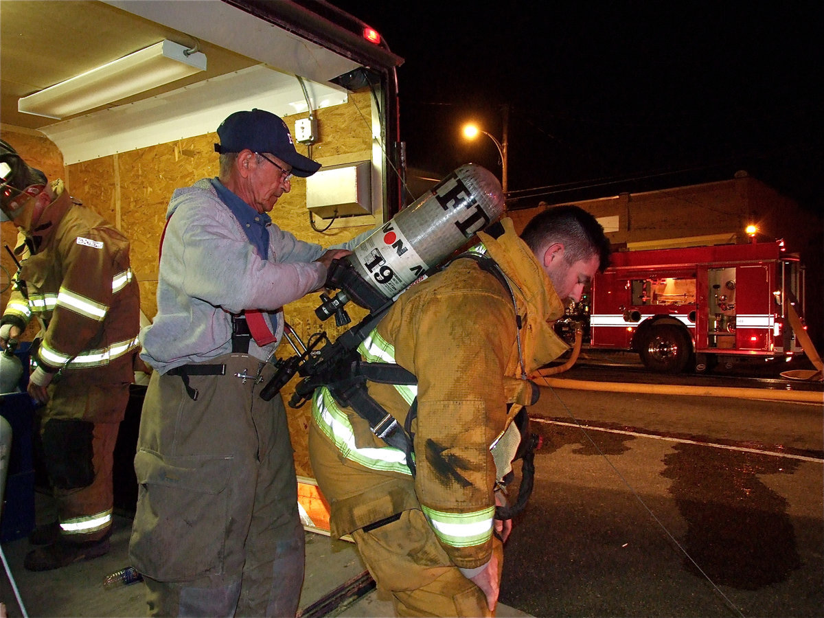 Image: Working together — Italy firefighter, Sal Perales, fits fellow firefighter, Russell Coers, with an air pack. Coers exhaustively went thru four different air tanks during the course of the fire.