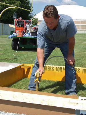 Image: Jon adds color — Italy ISD School Board member Jon Mathers spray paints a gold square in the far endzone near the scoreboard.