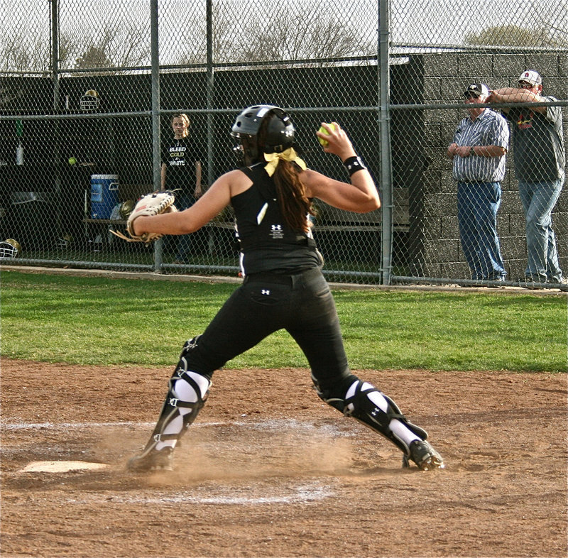 Image: Like we showed her — Lady Gladiator catcher, Alyssa Richards, shows the gun from behind the plate as her grandfather, Greg Richards, and father, Allen Richards, look on.