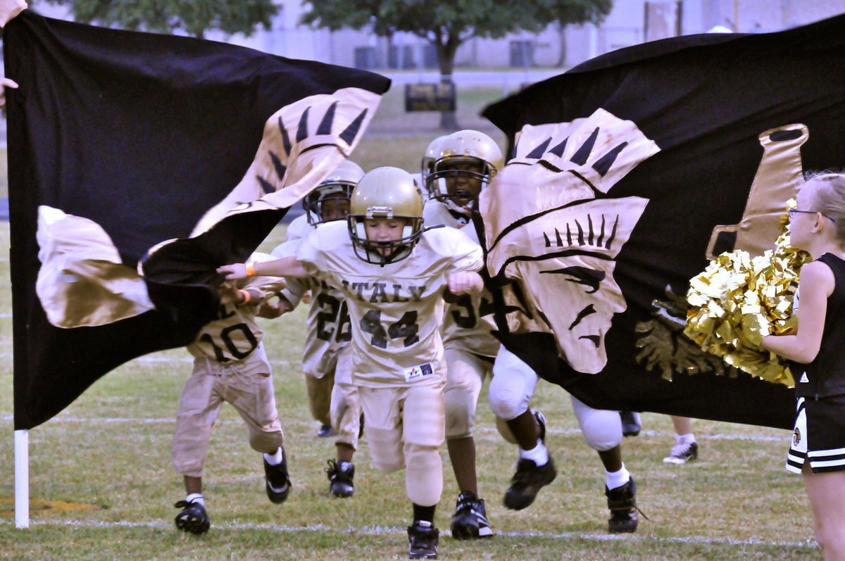 Image: Bryce brings friends — IYAA Cheerleader Madie Chambers cheers as Bryce DeBorde(44), Jaiden Barr(34), Joe Jackson(26) and Darrin Jackson(10) punch thru the Gladiators’ banner before knocking out the Hubbard Jaguars late in the fourth quarter.