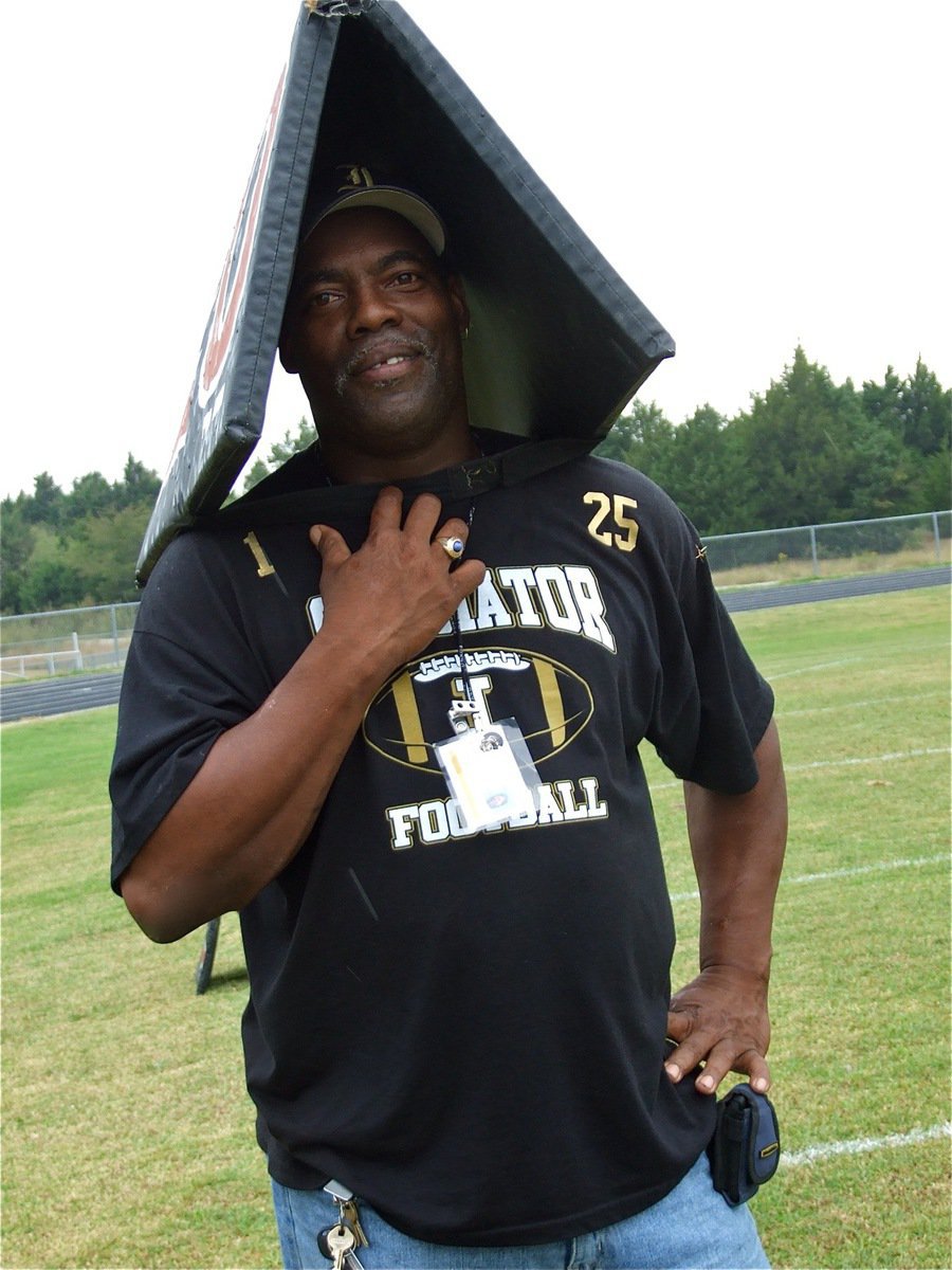 Image: Go away rain — A-Team head coach Ken Norwood demonstrates the latest fashion in football headwear by using a yard marker as an umbrella.