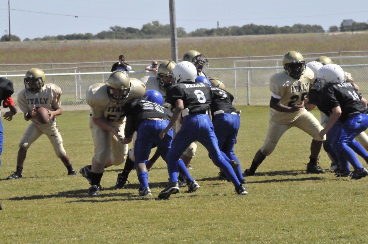 Image: Big Blocks — Austin Pittmon(50), center Austin Lowe(65) and Kenneth Norwood(25) fire off the line to block for Tylan Wallace(2) at quarterback.