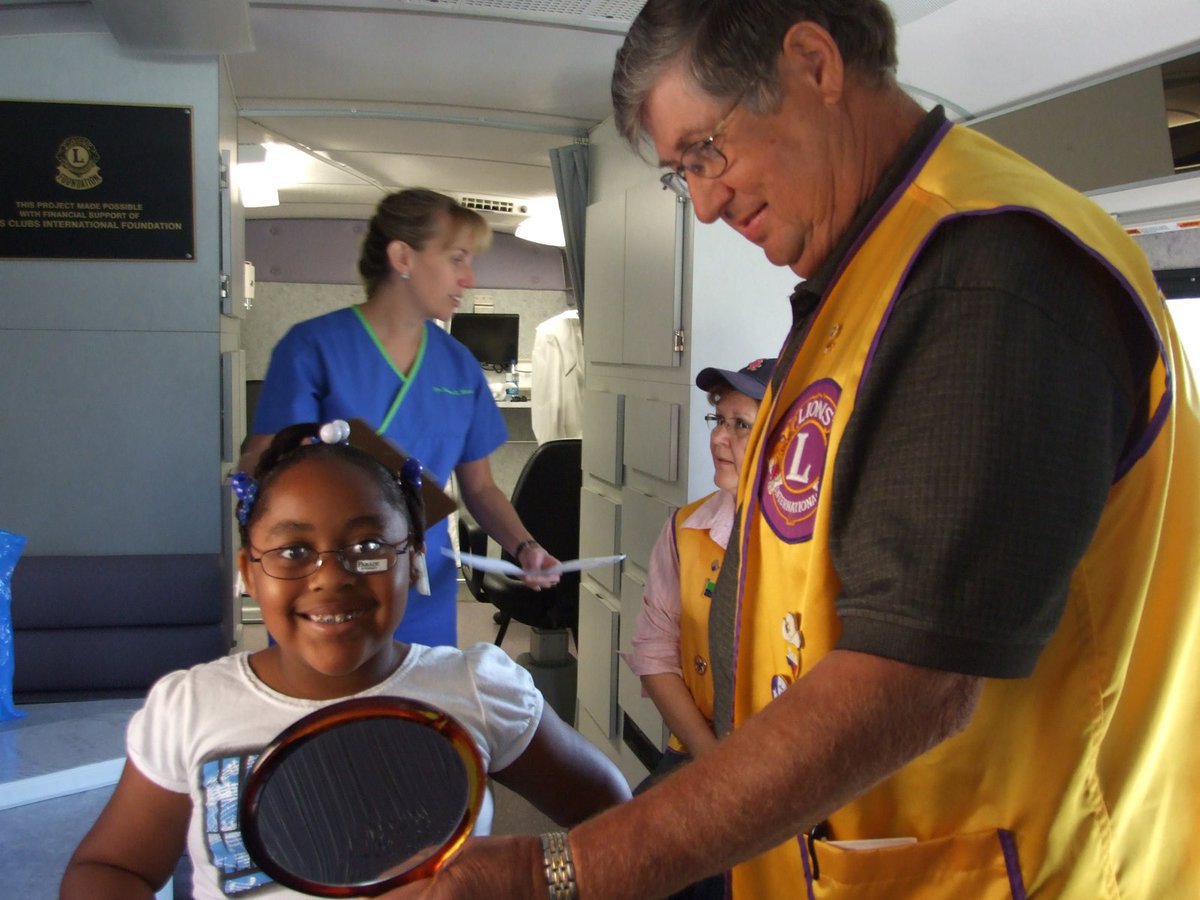 Image: Neil Roach  — Neil Roach, Lions Club member, is holding up the mirror for Alandia to help her make her choice of frames.