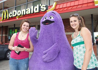 Image: Hey, Grimace! — Jamie Lopez and Brianna Perry are greeted by Grimace™ in front of the McDonald’s® in Italy during IYAA Sports Night on Wednesday.