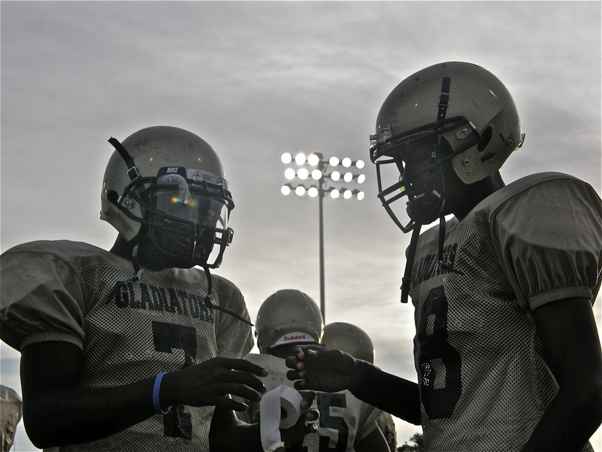 Image: Under the lights — Using the stadium lights as a lamp, Italy’s Junior Quarterback Jasenio Anderson (left) and Senior Wide Receiver Jon Isaac get taped up before Italy’s scrimmage against the Waco Reicher Cougars.