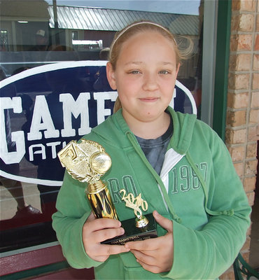 Image: Brycelen Richards — Brycelen Richards poses with her trophy in front of the Game On Athletics apparel print shop.