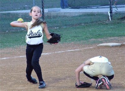Image: Heads up play — Pitcher Lacy Mott ducks down to give third baseman Karley Nelson a clear view of first base.