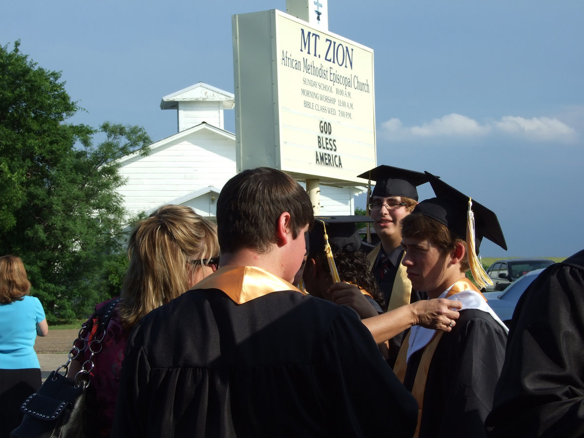 Image: Line up in order — IHS Counselor, Cari Cochran, help with collars and robes as the seniors line up at Mt. Zion.