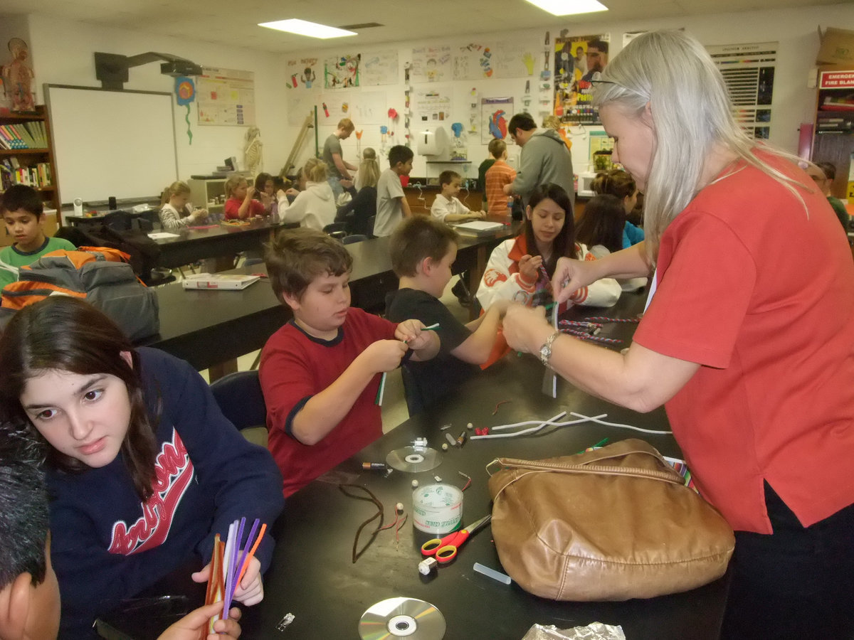 Image: Twist Like This — Miss Campbell is helping students to twist the pipe cleaners into Jitterbug legs.