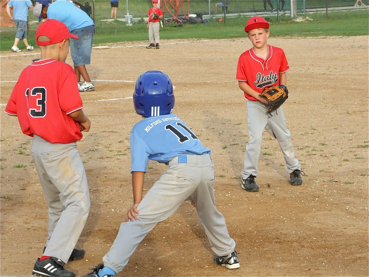 Image: I dare you — With his rally cap flipped up, Reese Janek dares a Milford runner to try for second while Janek’s teammate, Cornelius Jones, waits for the throw.