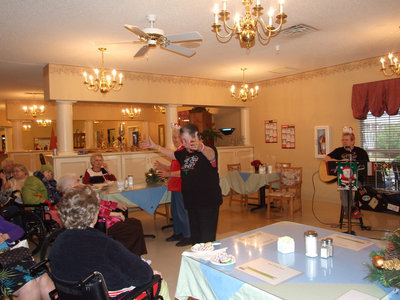 Image: Bobbie directs the singing — Bobbie is helping residents sing Christmas songs.