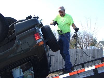 Image: Mr. Helms In Action  — Mr. Keith Helms begins unloading a smashed vehicle from his wrecker. Mr. Helms opted not to attempt turning the auto over on the bridge and instead set it upright back at the shop.