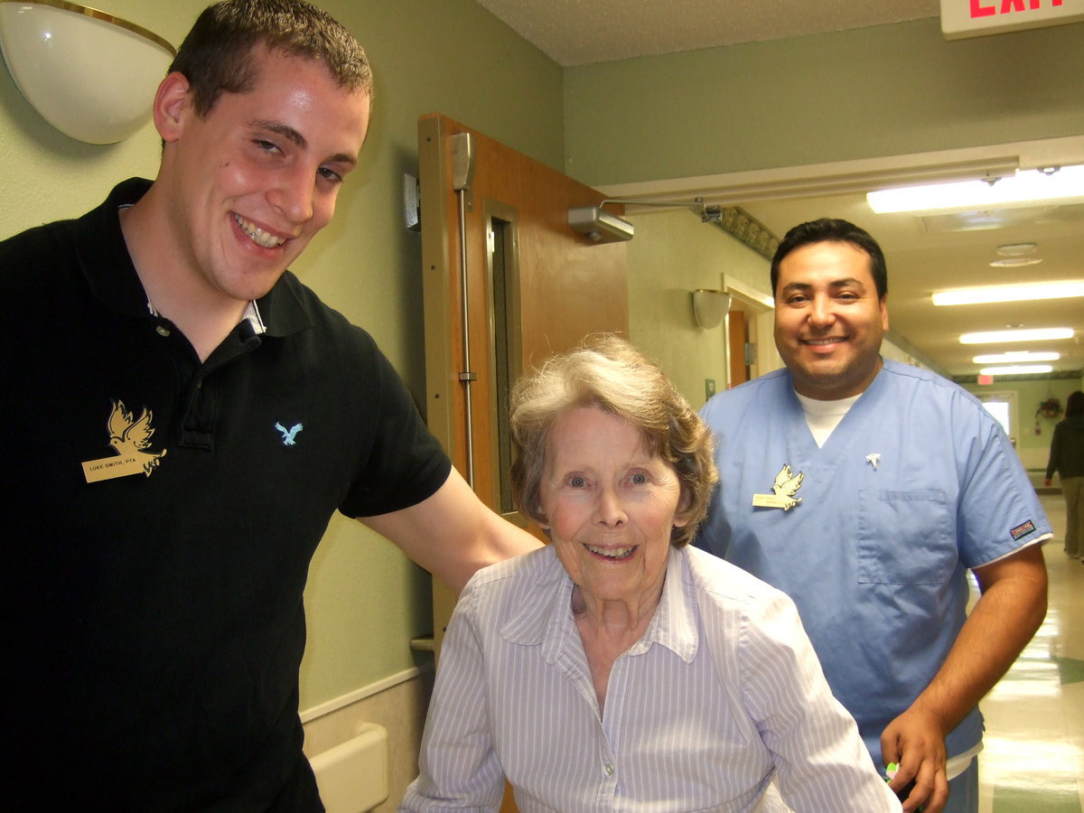 Image: Luke, Francis and Elias — Luke Smith (physical therapist assistant), Francis Davidson and Elias Perez (physical therapy assistant). Luke and Elias are helping patient Francis with her therapy workout.