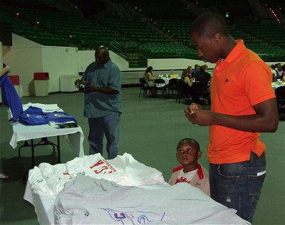 Image: Anything in a gold? — Jasenio Anderson looks over the FCA Victory Bowl shirt selection with his nephew, Ty Anderson, and father Willie Henderson.