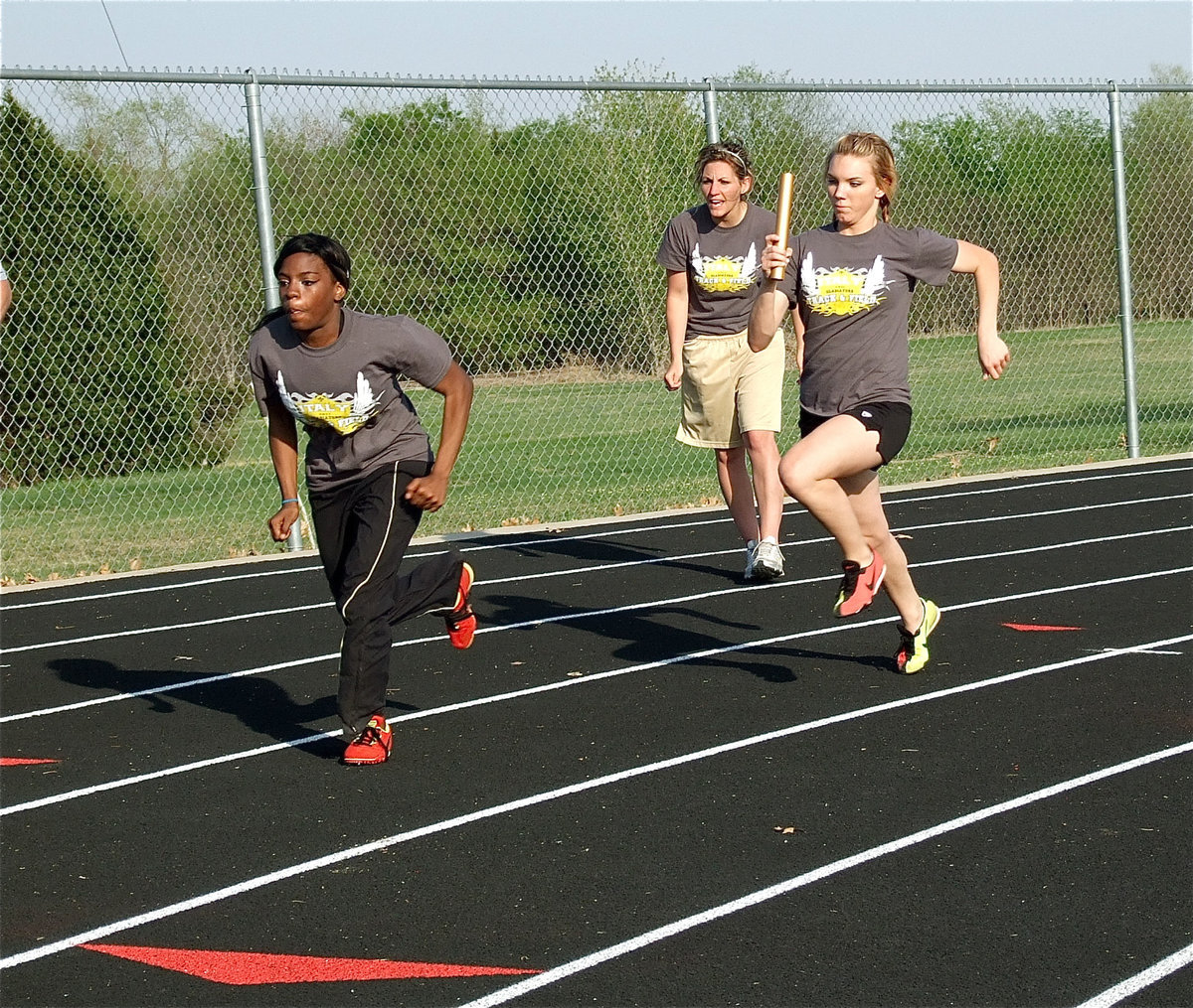 Image: Harder than it looks — Coach Heather Richters instructs Kendra Copeland and Sierra Harris while they work on their handoffs.