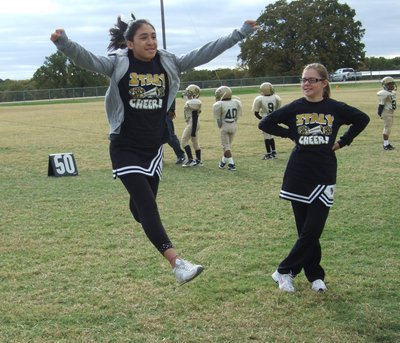 Image: Lizzie leaps — IYAA cheerleader Brooke DeBorde looks on with a smile as fellow cheerleader Lizzie Garcia touches the sky.