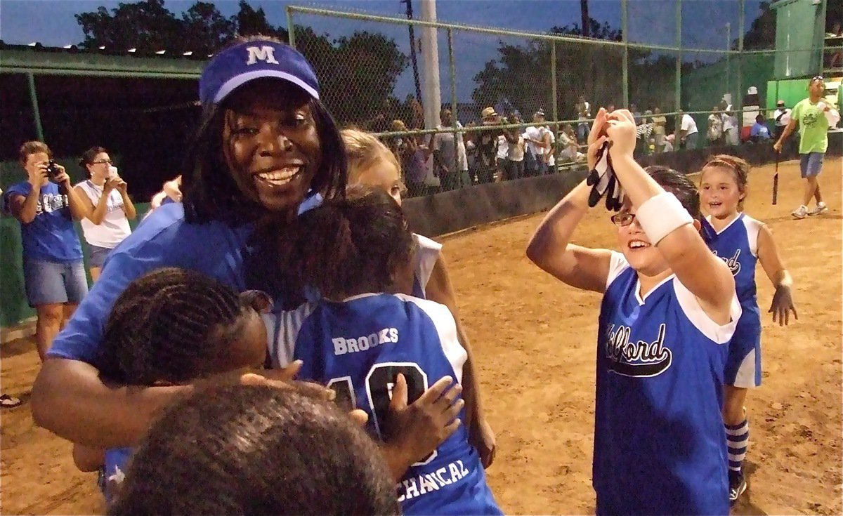 Image: We’re the champs! — Milford’s assistant coach Veronica Rankin gather’s as many Lil’ Dogs as she can hold in her arms following the dramatic extra inning win over Ferris.