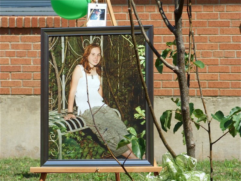 Image: A portrait of Samantha Nance on display next to her tree — A portrait of Samantha (Shelley) Nance stands next to the tree dedicated in Shelley’s memory that was planted in the courtyard at Italy High School to commemorate her amazing life that ended much to soon in the fall of 2009.