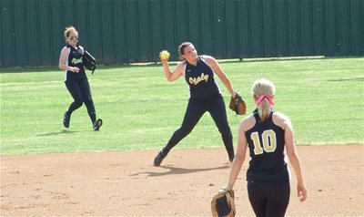 Image: Cori hurries — Second baseman Cori Jeffords tries to throw out a Lady’ Jacket runner as Bailey Bumpus backs up the play from centerfield and pitcher Courtney Wesbrook looks on.