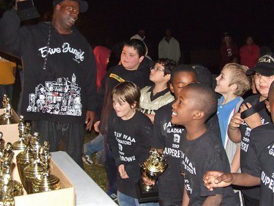 Image: Can’t wait any longer — IYAA B-Team Head Coach Ken Norwood hands out the trophies to his eager players.