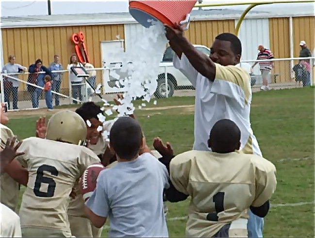 Image: B-Team gets the ceremonial bucket of ice after going undefeated — IYAA B-Team Assistant Coach Edwin Wallace takes the bucket of ice from his sneaky players and turns the tide on them after their 32-0 win over Rice. B-Team finished the regular season as 7-0 division champs and will compete for the conference championship in Rice next Saturday along with the IYAA C-Team and hopefully the IYAA A-Team.