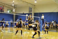 Image: Lady Gladiators vs Lady Bulldogs — Two Lady Gladiators elevate side by side at the net to block a Lady Bulldog hit.