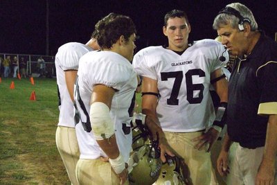 Image: Coach Coleman and players — #76-Jeff Claxton (Sugar), #50-Ethan Simon, #66-Trent Morgan work with Coach Coleman on the sidelines.