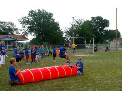 Image: This obstacle course requires the students to jump over the tube, zig zagging  through the cones, jumping hurdles, kicking a ball through the cones and finally throw the football through the hoop.