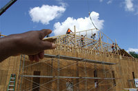 Image: Mr. Ervin Green, Sr. directs the camera toward the roofers atop the new church as the first rafter is set in place.