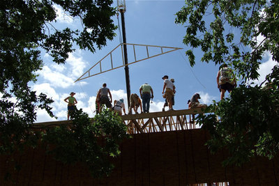 Image: Workers are framed within tree leaves and branches while framing the roof of the new church.