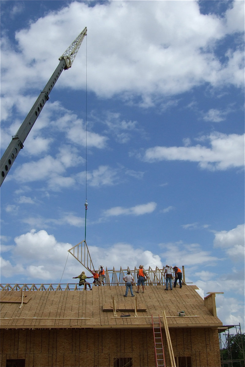 Image: A large crane continues to lower rafters to the awaiting roofers.