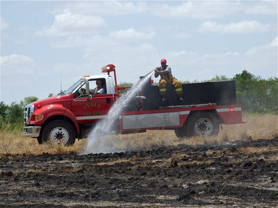 Image: Italy firefighter, Randy Boyd, drives while fellow firefighter, Jackie Cate, pours more water on a nearby pasture.