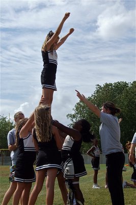 Image: A-Team cheerleaders perform a stunt as Hannah Haight raises her arms in triumph. Cheer Coaches Brooke DeBorde and Darla Wood monitor the move.