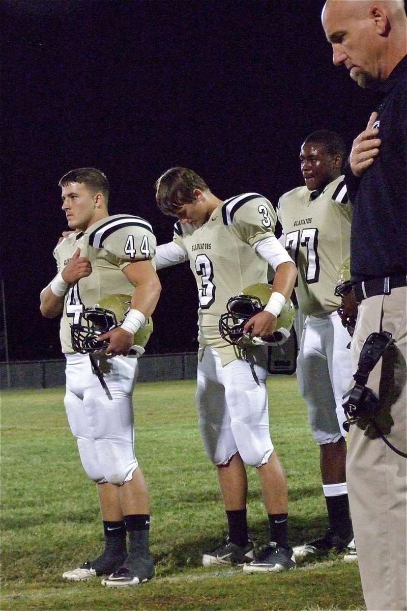 Image: Ethan Saxon(44), Jase Holden(3), Larry Mayberry, Jr.(77) and Coach Jeff Richters show respect before the game.