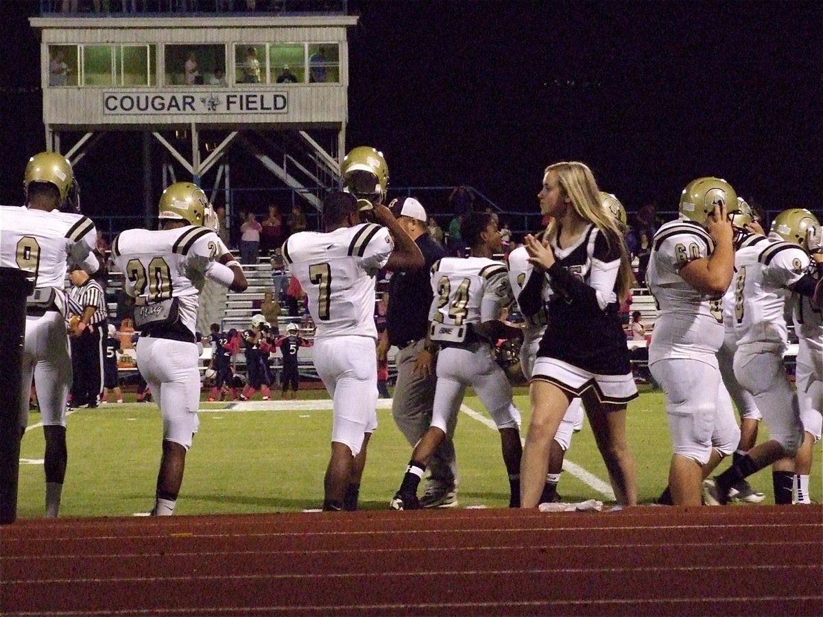 Image: Devonta Simmons(9), Trevon Robertson(20), Paul Harris(7), Eric Carson(24), Jamal Lewis(11), Kevin Roldan(60), Hayden Woods(8) buckle their Gladiator helmets on tight as they prepare to step onto Cougar Field with some encouragement from Kelsey Nelson.