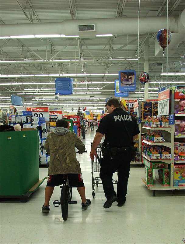 Image: How often do you get a police escort while riding a bike around Walmart? Officer Eric Tolliver keeps pace with Austin while he tries out his new bicycle.