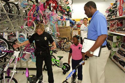 Image: Henry E. Gasaway, an assistant manager at Walmart #260 in Waxahachie, assists Officer Tierra Mooney and Stafford Elementary 1st grader Mariah Davis in picking out just the right bicycle.