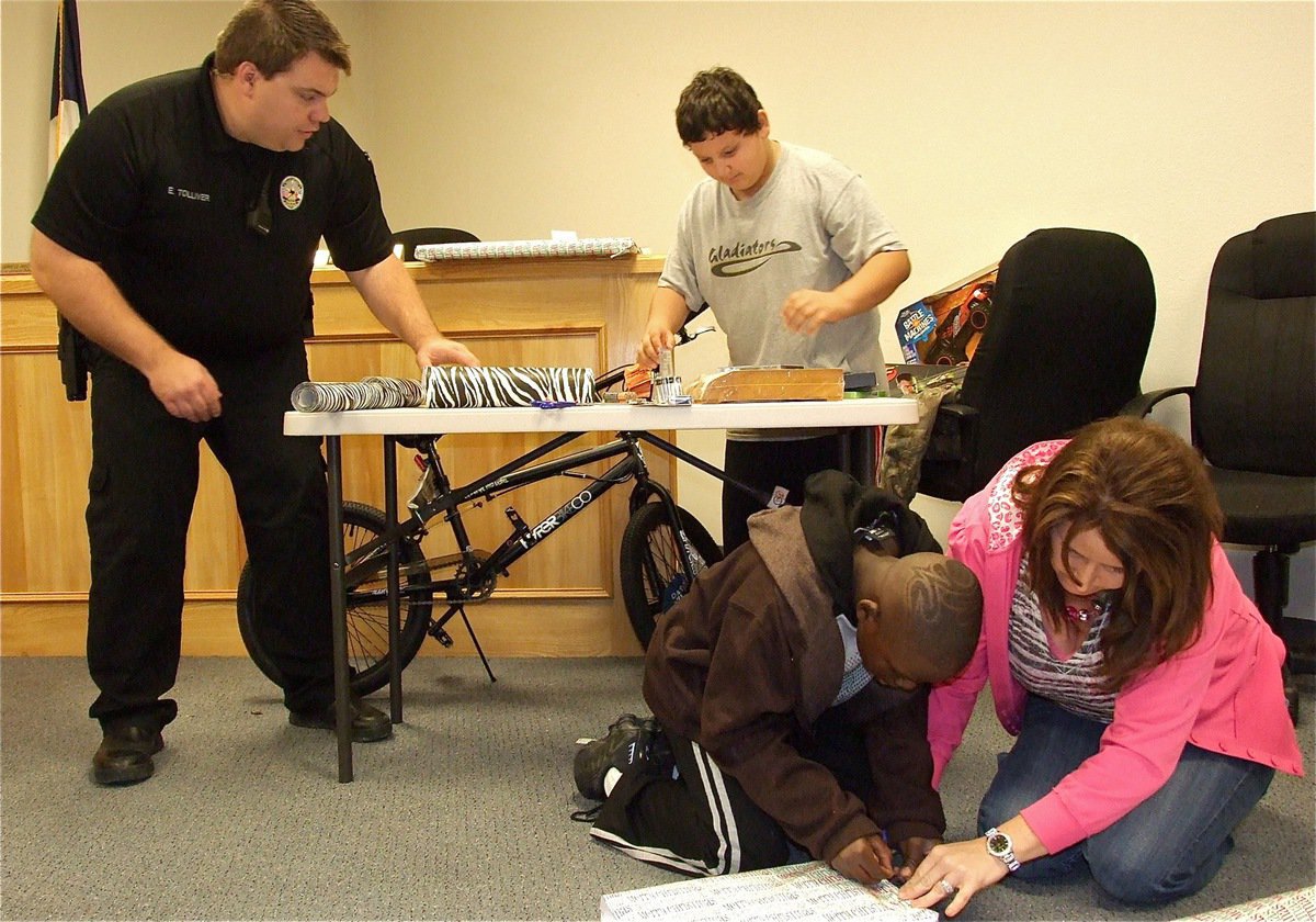 Image: Officer Tolliver helps Austin put the final touches on a wrapped present while Deonna Padilla assists Byron with the wrapping of one of his gifts. 