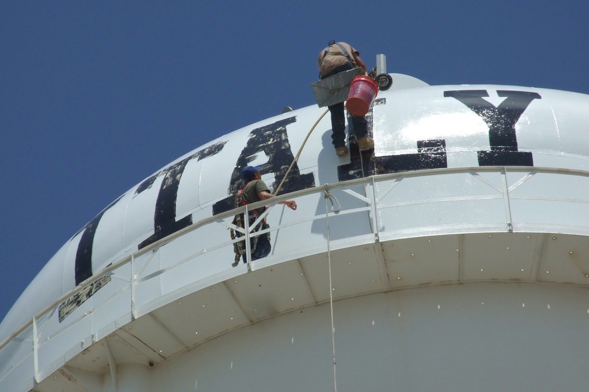 Image: A crew member from R &amp; K Sandblasting &amp; Paint scales the the top of the tower.